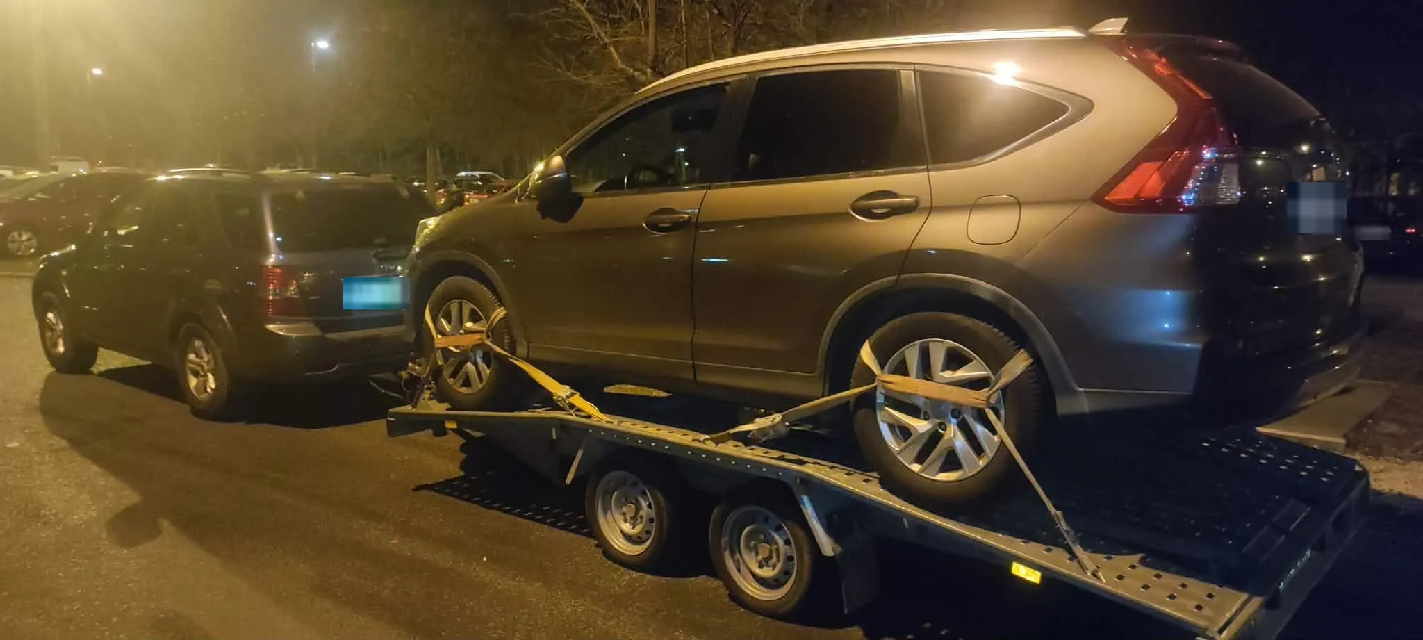Éjszakai autómentés – sérült SUV hevederekkel rögzítve az autószállító tréleren